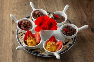 A plate with four bowls of desserts and a flower